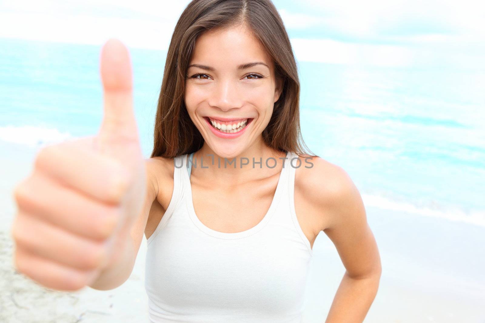 Happy asian woman giving thumbs up success hand sign outside on beach smiling joyful. Sporty fit young mixed race Chinese Asian Caucasian female fitness model outdoors.