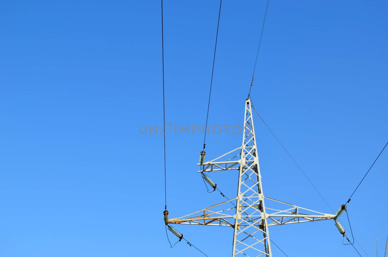 High-voltage electricity wires and poles in background of bluse sky with clouds.