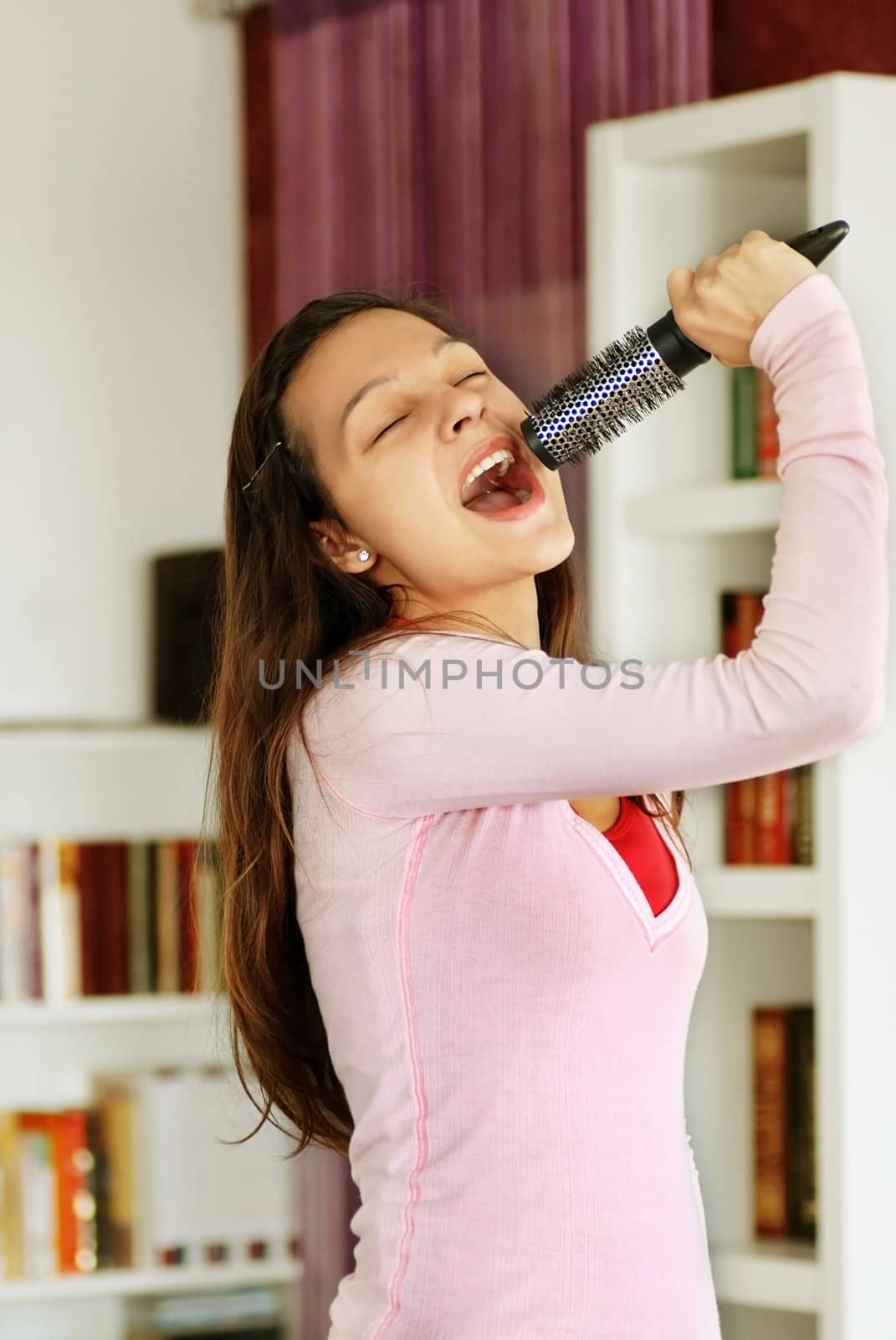happy caucasian teenage girl singing with a hairbrush as a microphone at home