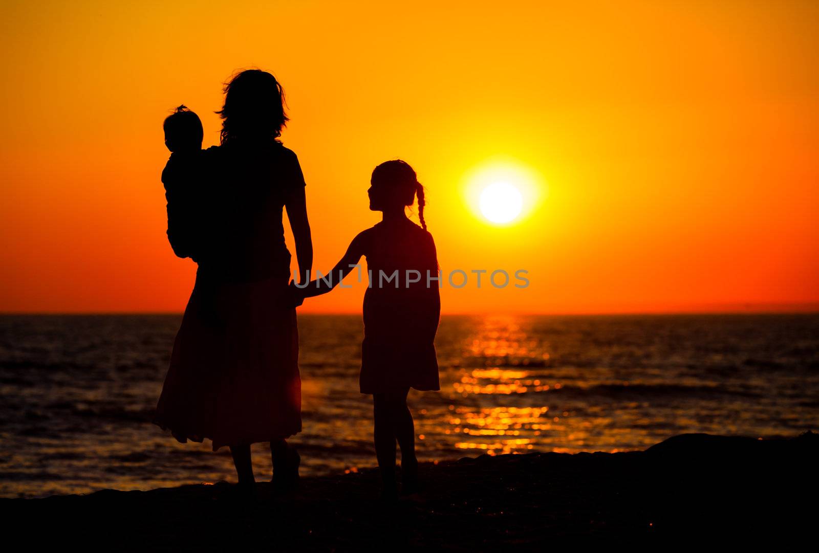 Mother and her kids silhouettes on beach at sunset