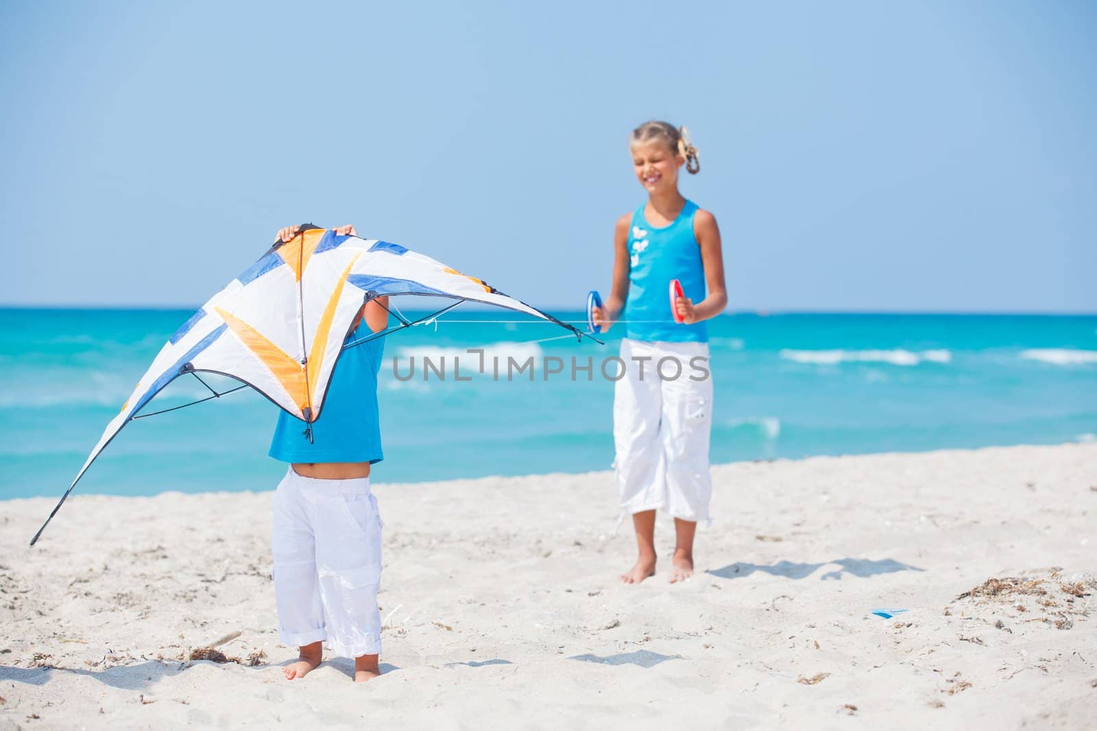 Young cute girl playing her brother with a colorful kite on the tropical beach.