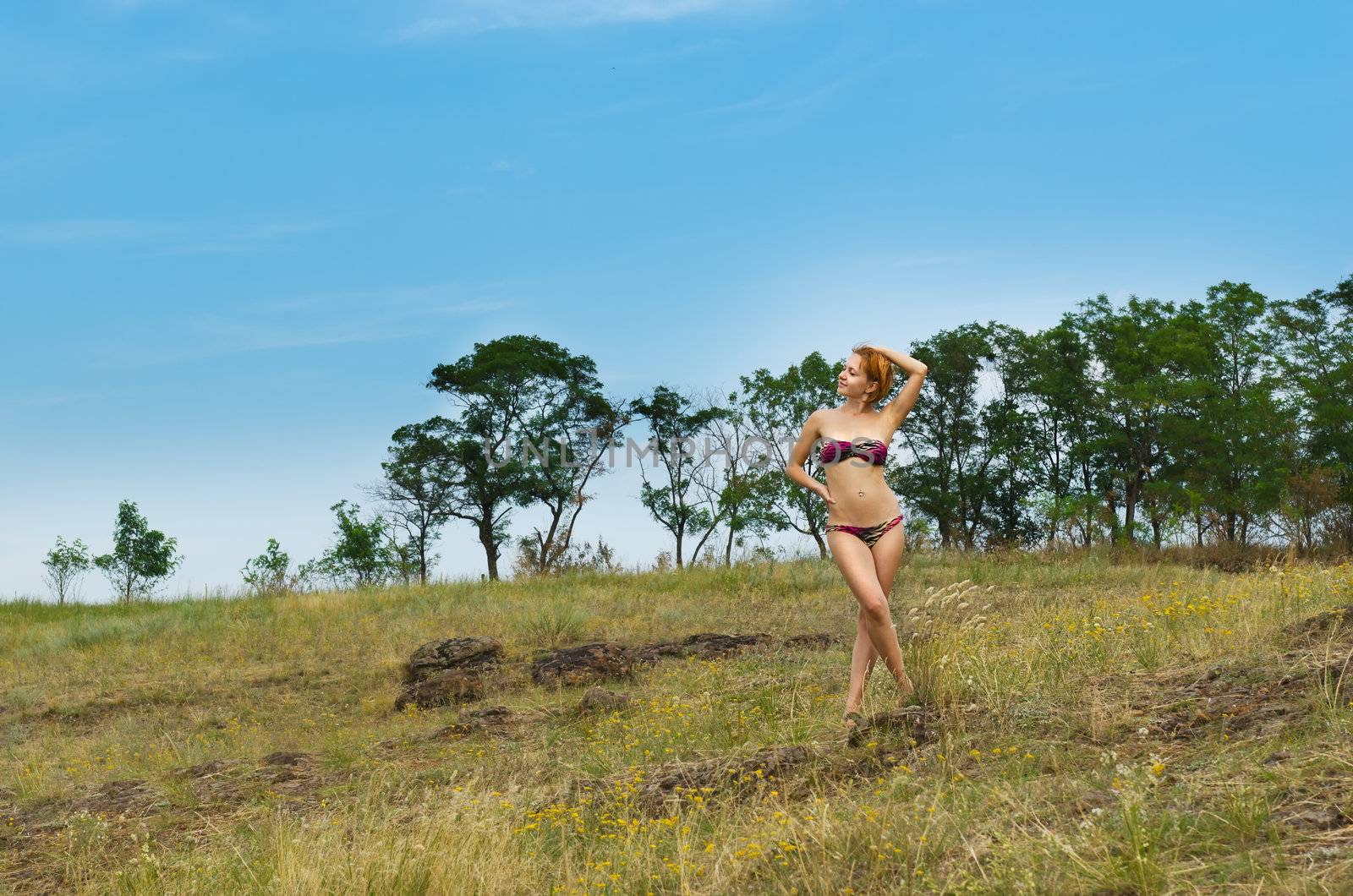 Beautiful red woman wearing bikini posing with forest in the background