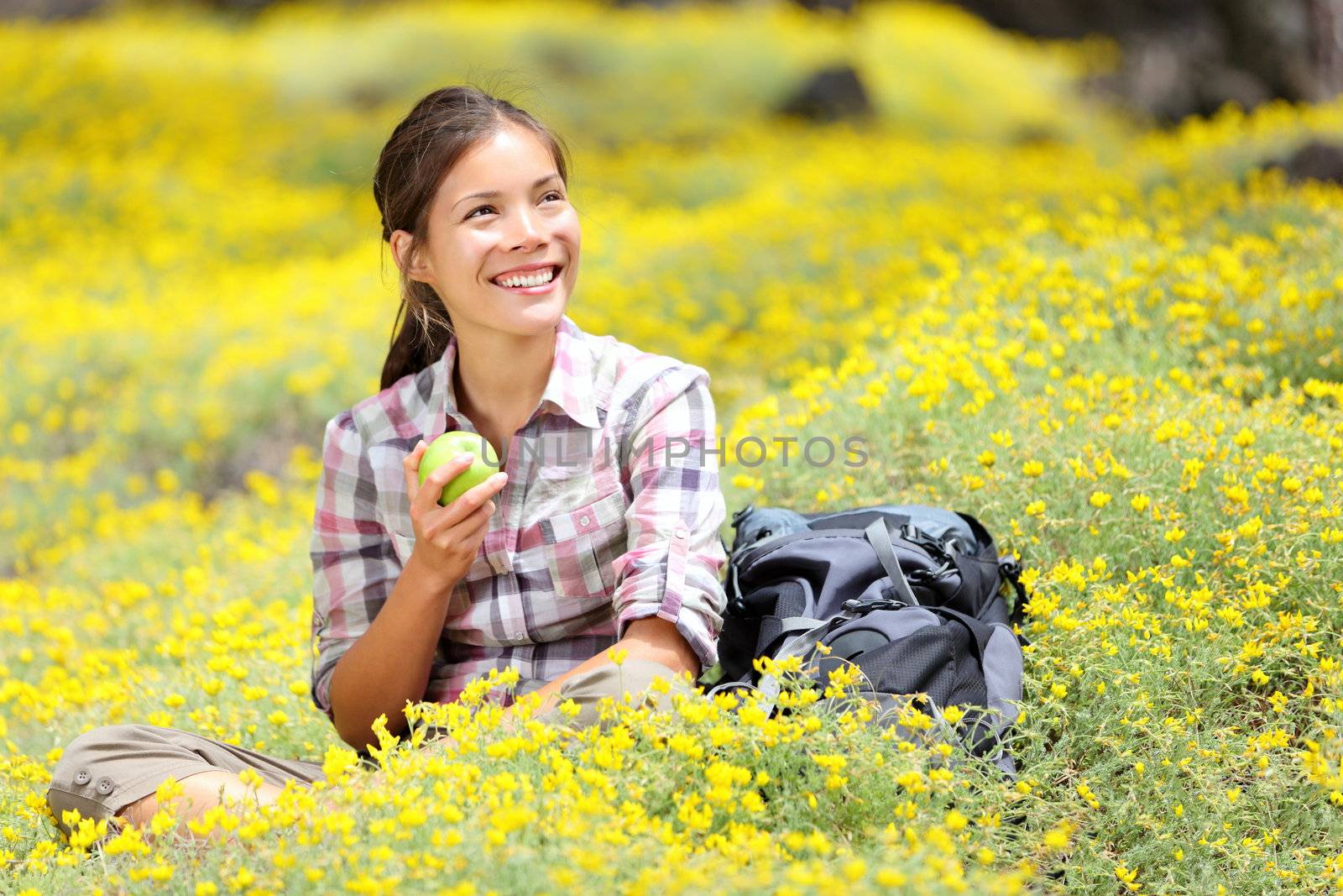 Hiking girl in spring sitting in forest floor flowers. Beautiful woman hiker smiling happy eating an apple during break. Mixed race Asian / Caucasian woman outdoor.