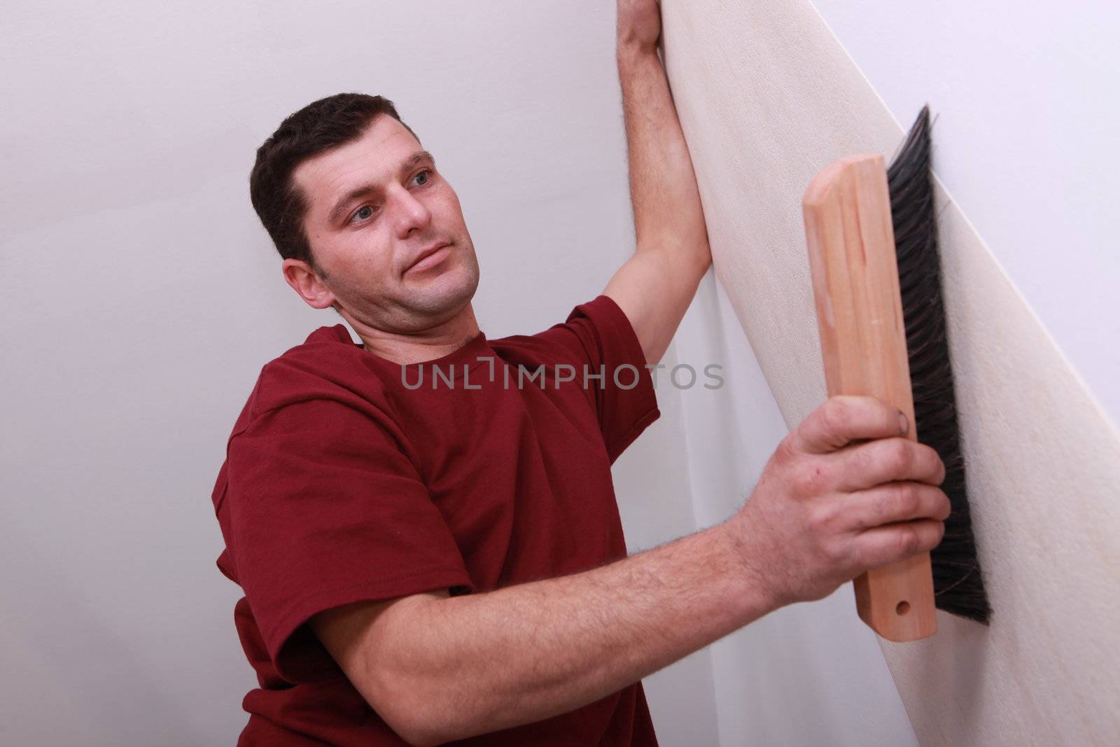 Low shot of a man smoothing wallpaper with a large brush by phovoir