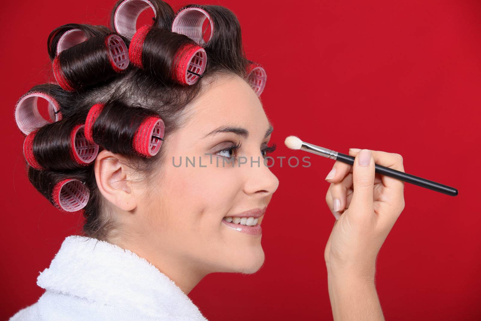Woman with hair curlers applying make-up by phovoir