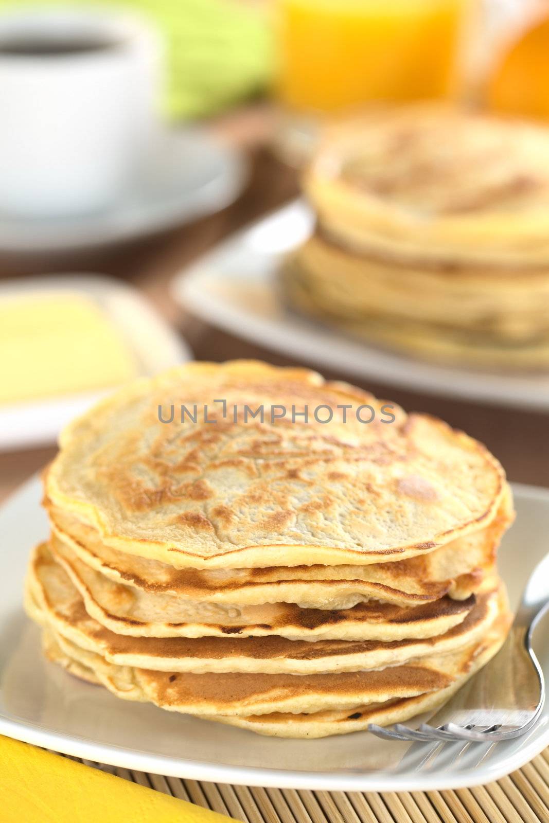 Fresh homemade pancakes with coffee, orange juice and butter in the back (Selective Focus, Focus on the front of the upper three pancakes) 