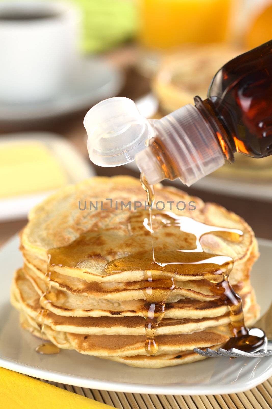 Pouring maple syrup on fresh homemade pancakes (Selective Focus, Focus on the front of the upper three pancakes)