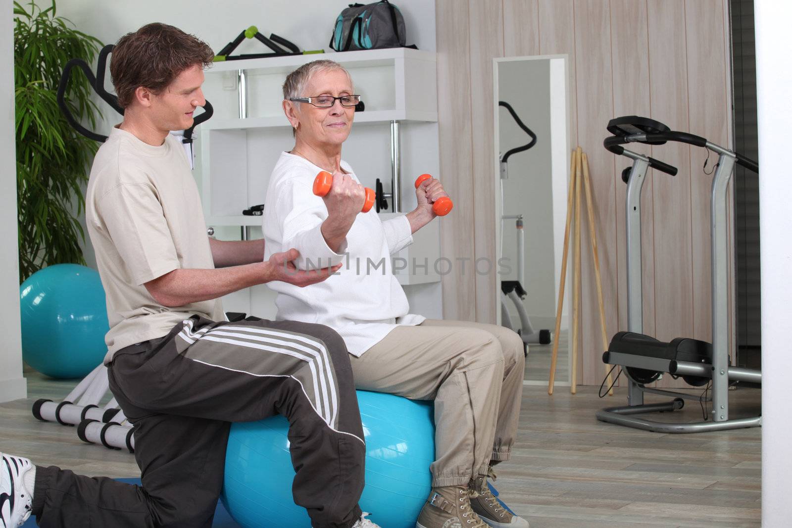 Older woman working out with a personal trainer at the gym by phovoir