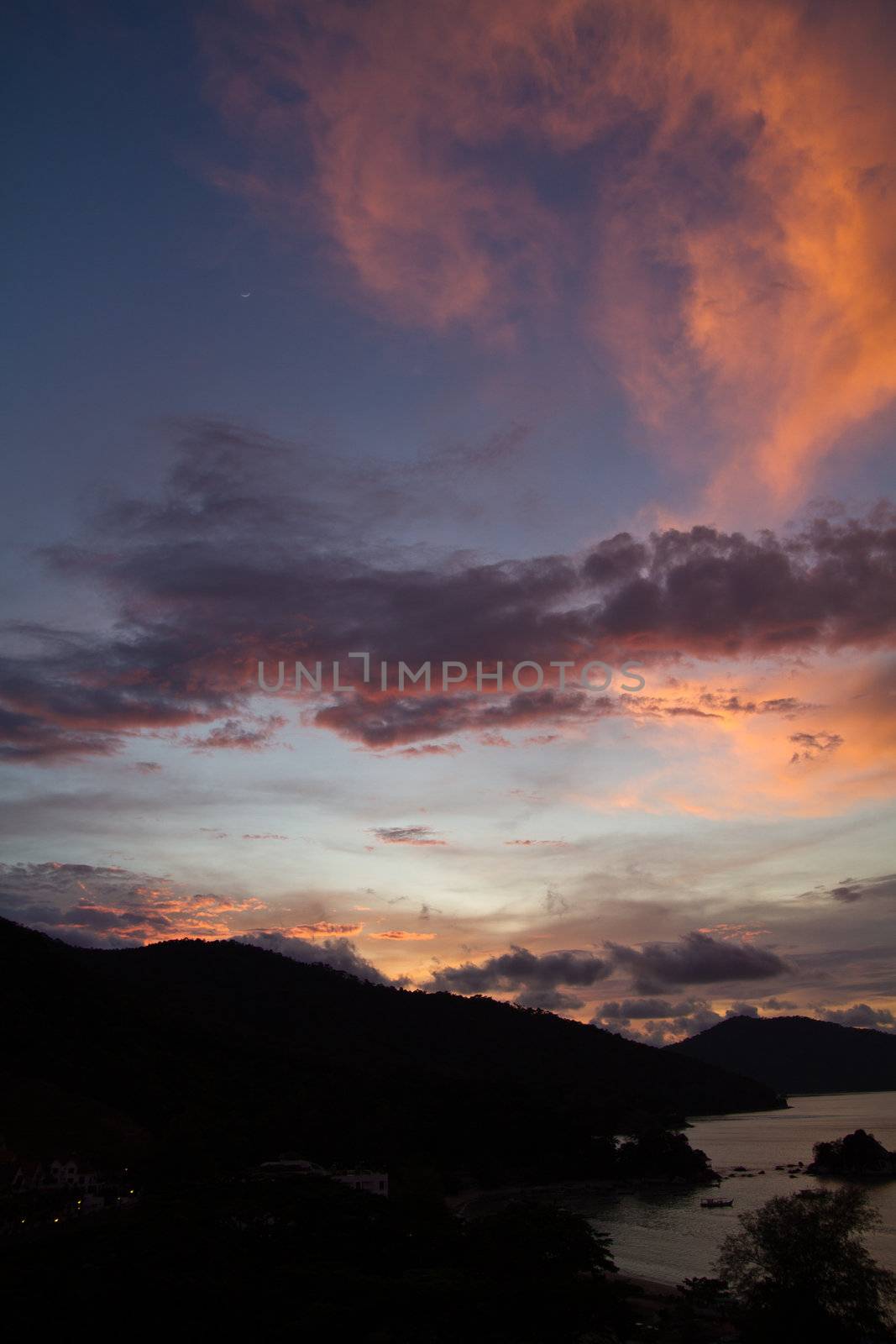 Sunset over the hills at Batu Ferringhi Bay Penang Malaysia with silhouette of the hills and bay coastline in portrait orientation