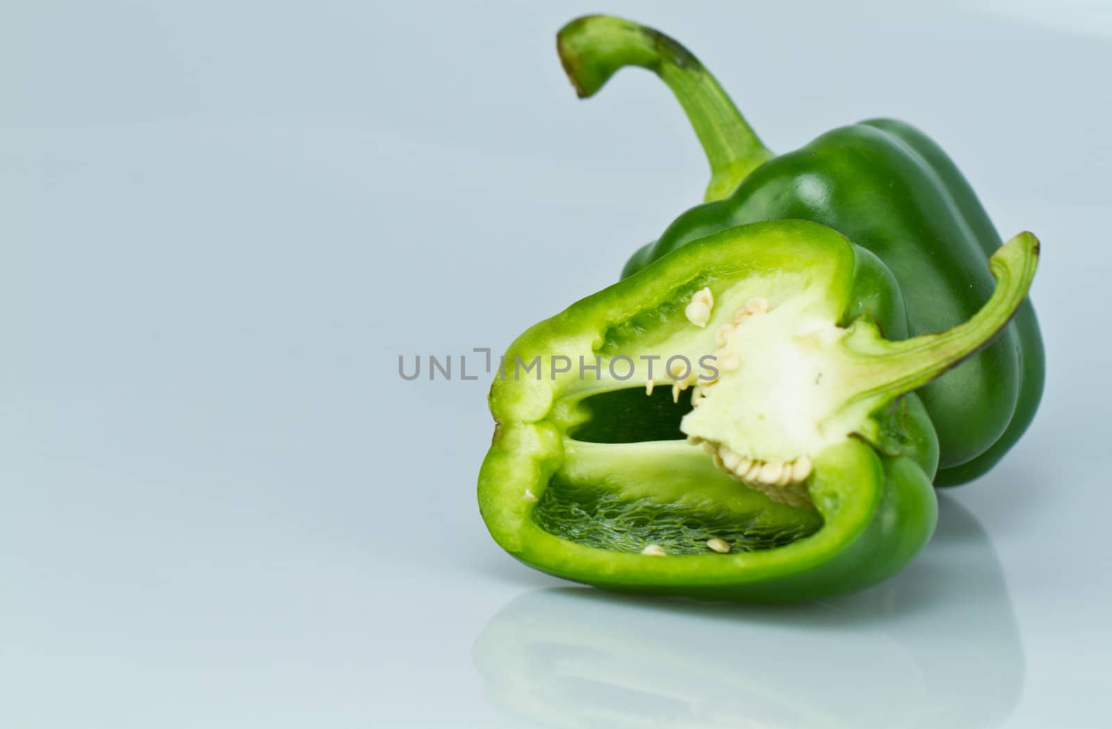green capsicum with one cut open on bluish surface and background in landscape orientation with copy space