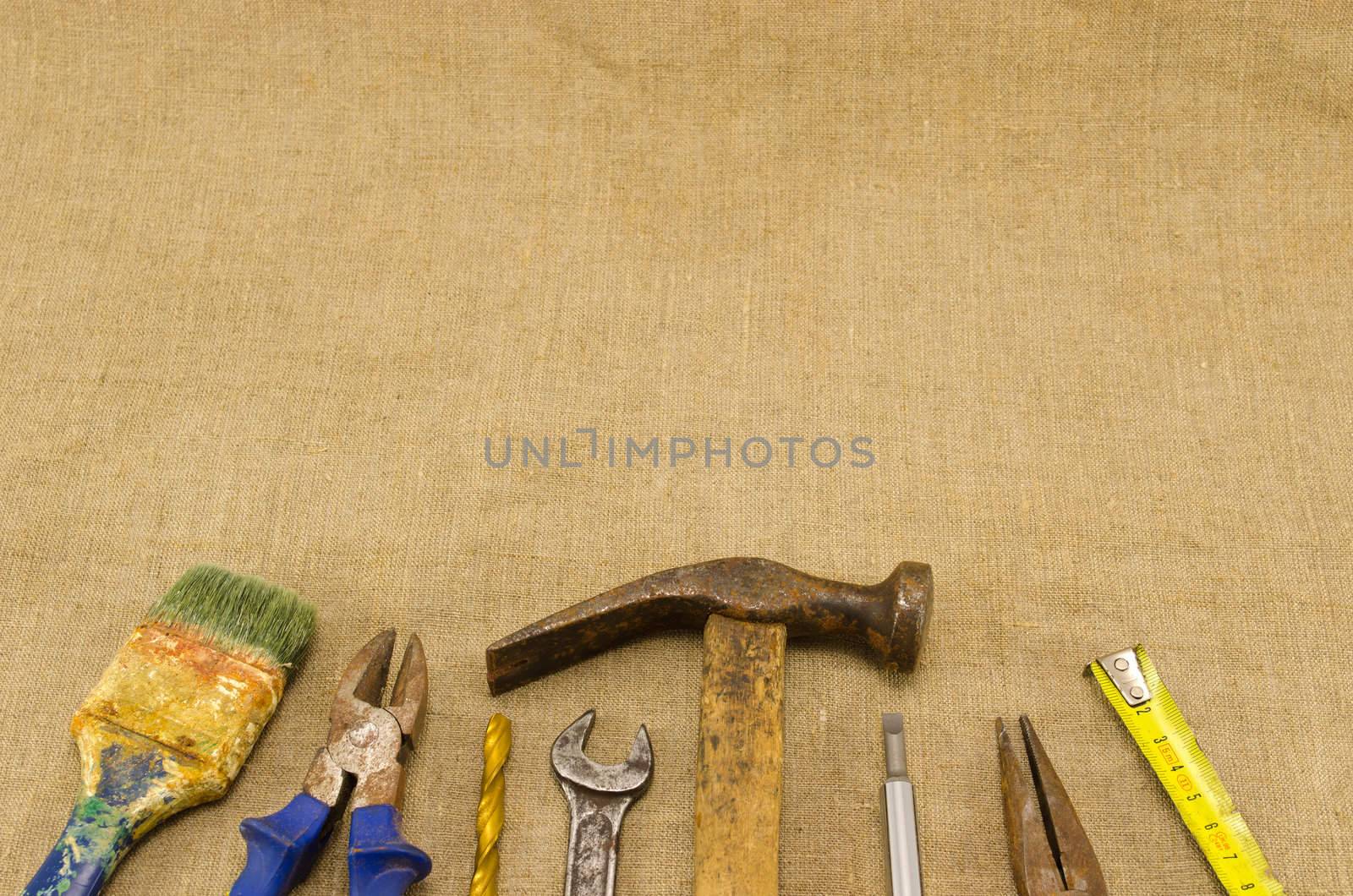 different retro rusty construction work tools hammer meter chisel wrench pincers screwdriver brush bit on linen cloth cloth background.