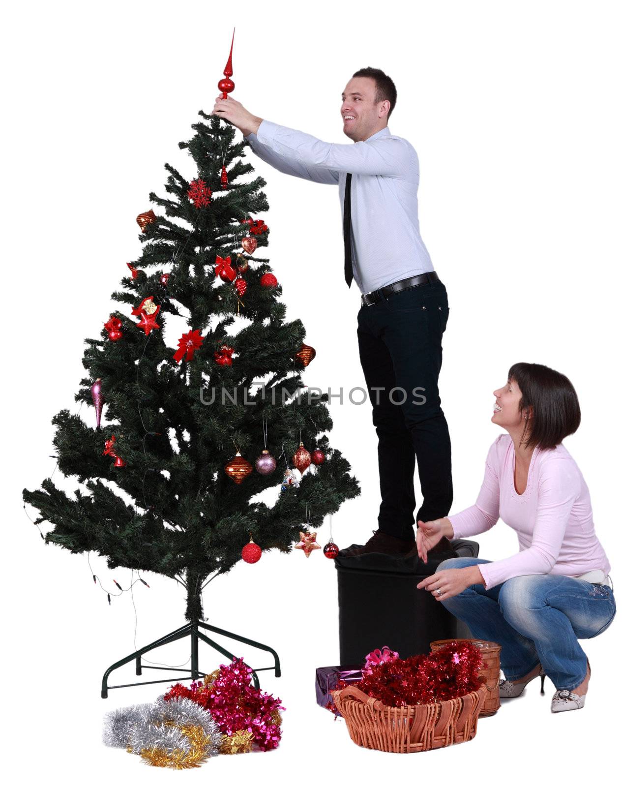 Studio shot of a young couple decorating the Christmas tree, against a white background.