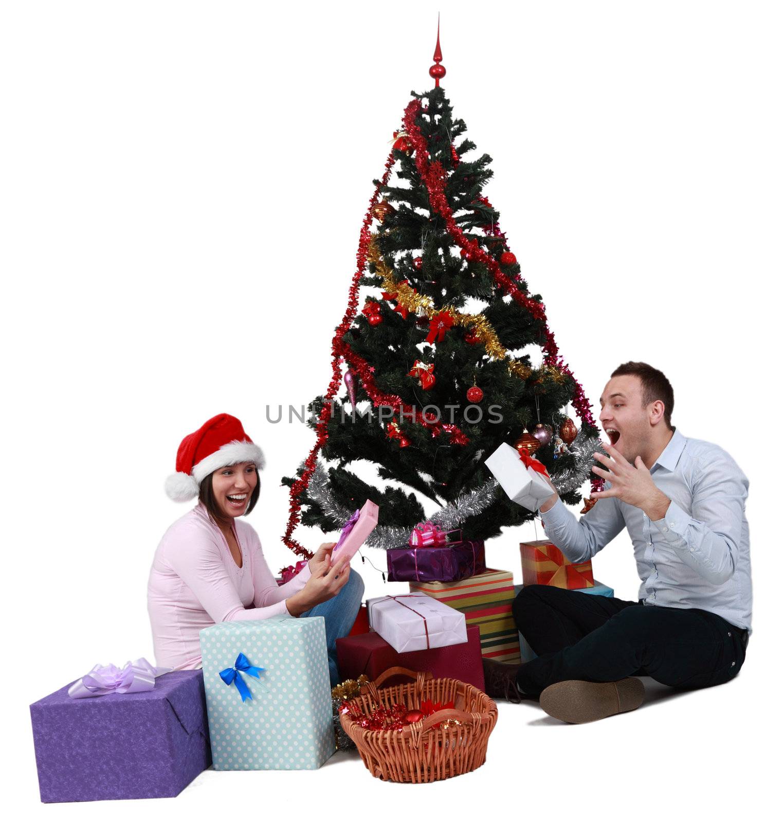 Studio shot of a young couple enjoying the gifts in front of the Christmas Tree, against a white background.