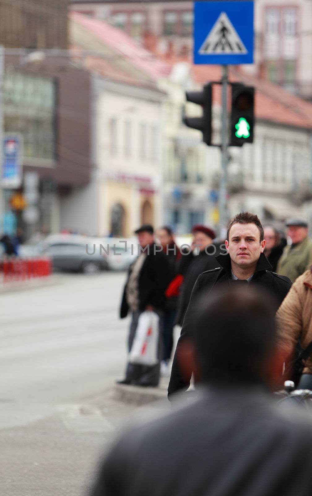 Image of a young businessman crossing a street in a city.Selective focus on the man with blur on the others people.