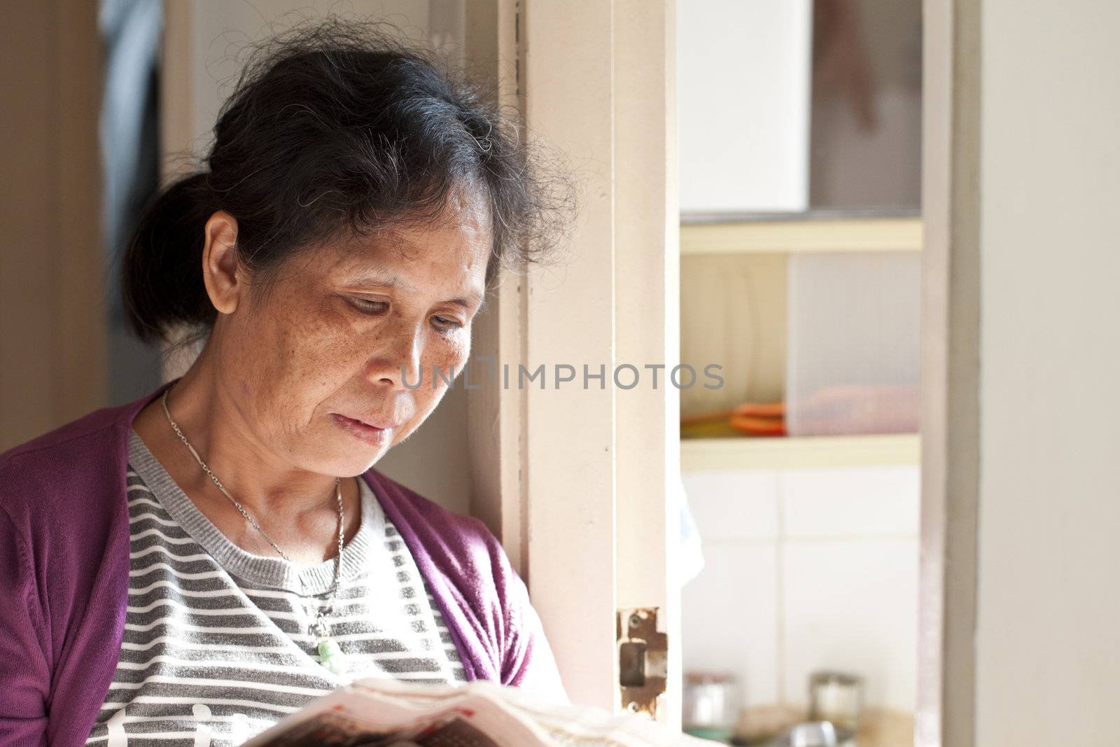 A 50s asian woman reading newspaper at home