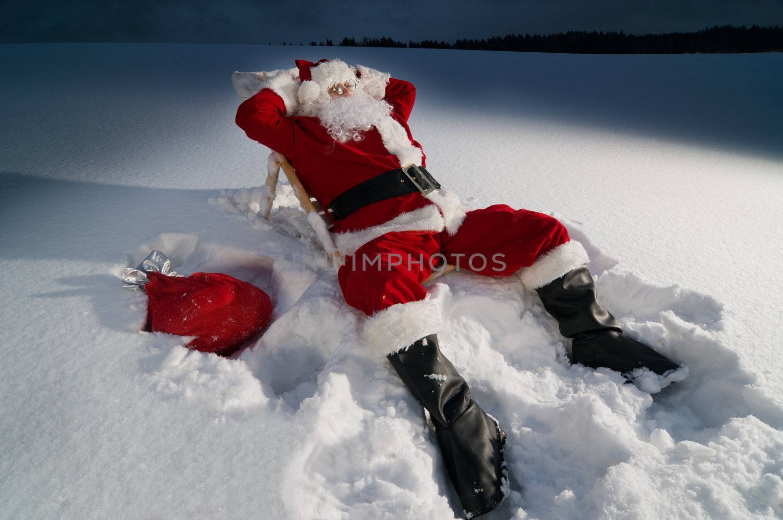 Santa claus relaxing on a sunbed in snow at night