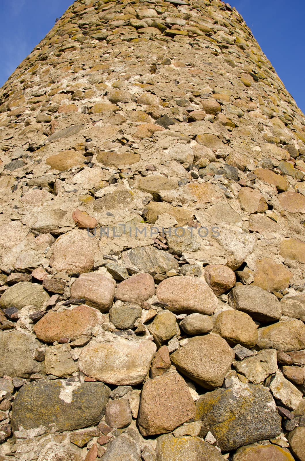 Fragment of tall wall made of many different shape stones rising in blue sky.