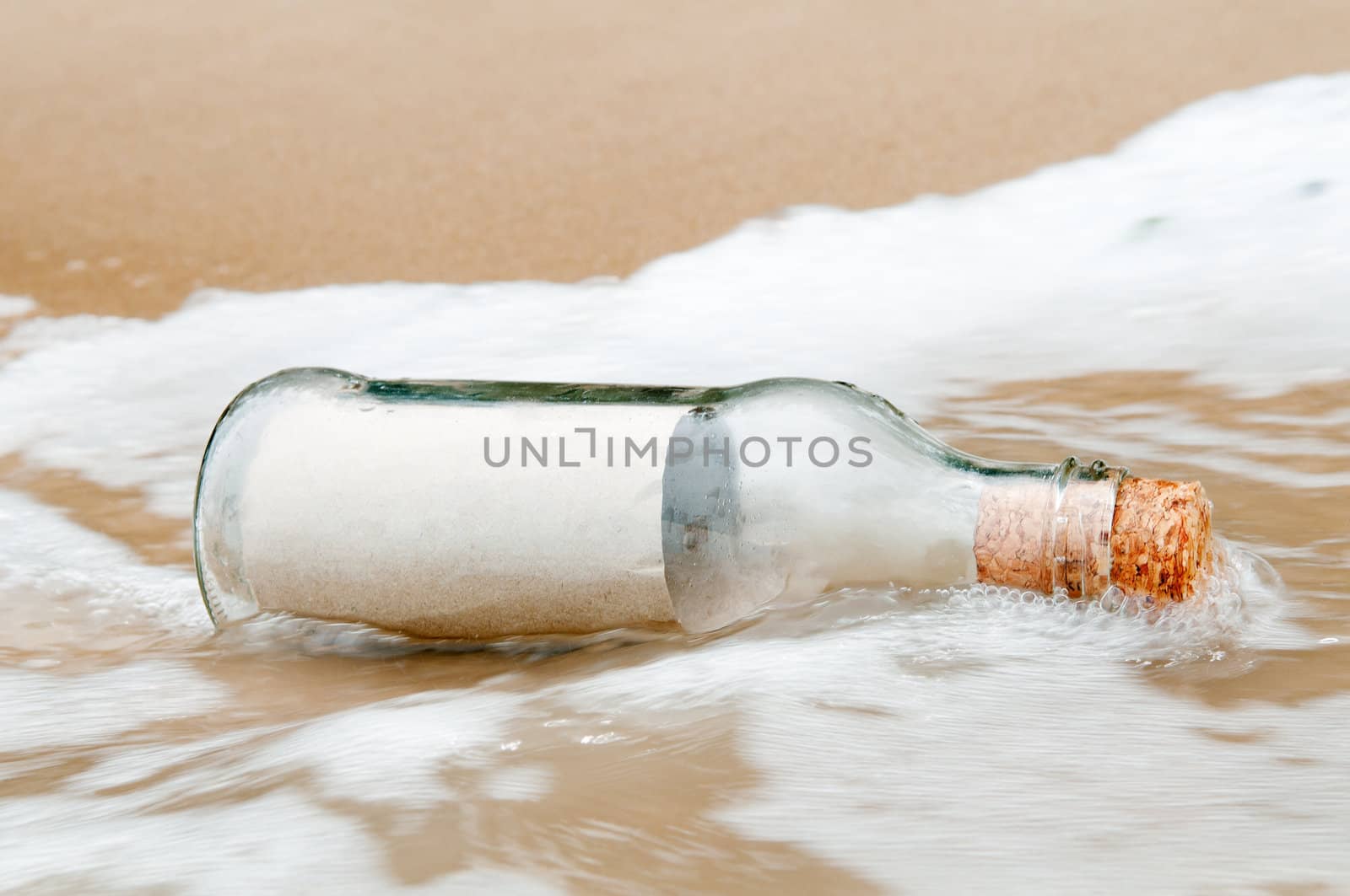 Blank brown paper in glass bottle being swept ashore on the beach.