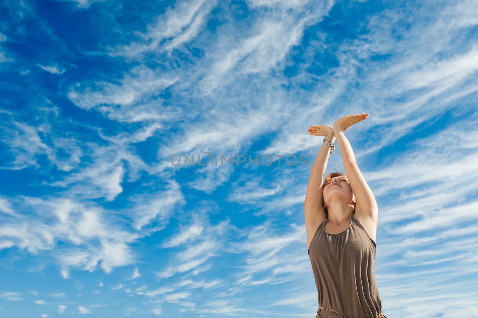 Beautiful young dancer performing yoga-dance outdoors with blue sky and clouds in the background