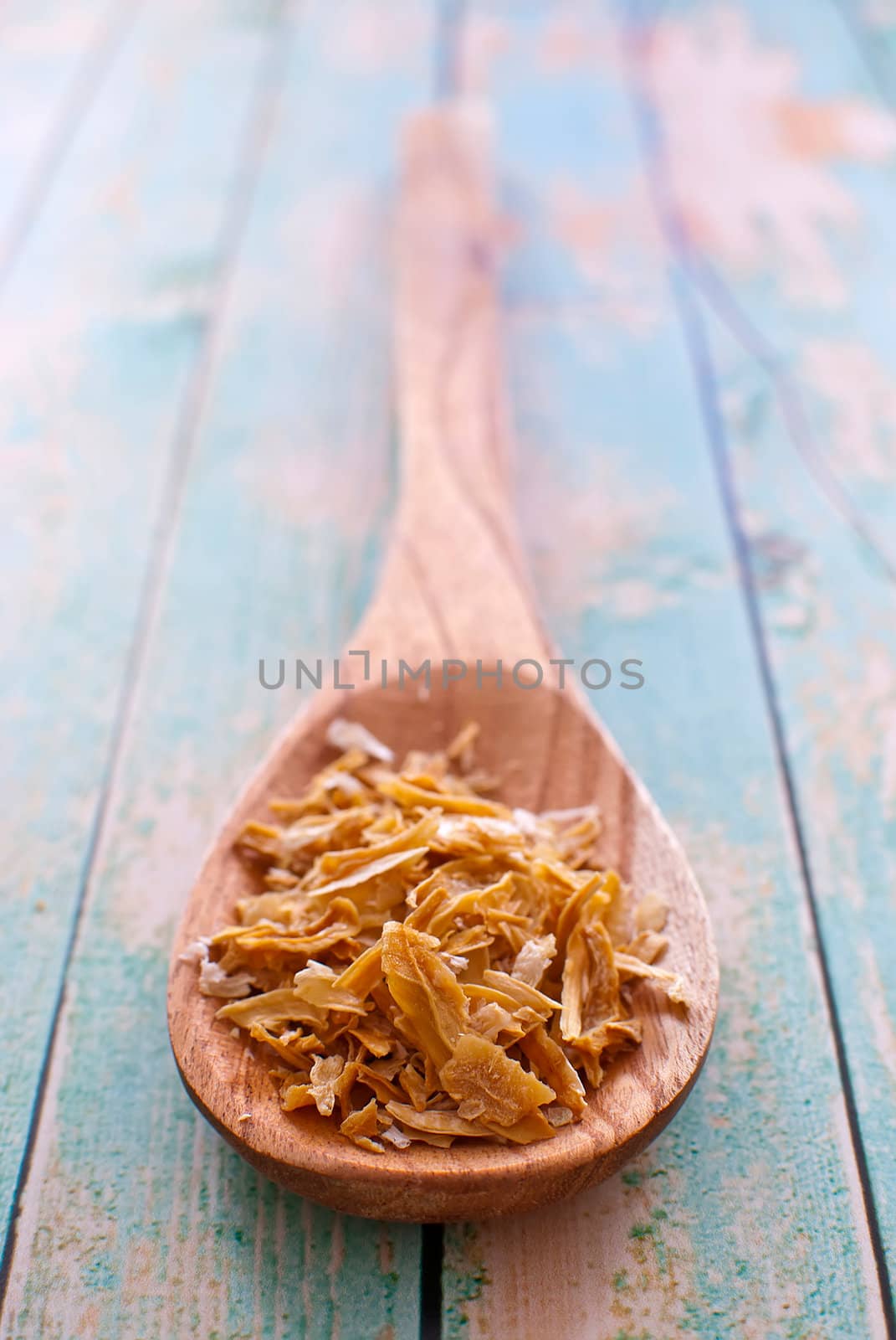 dried onion flakes in wooden spoon over wood background - selective focus