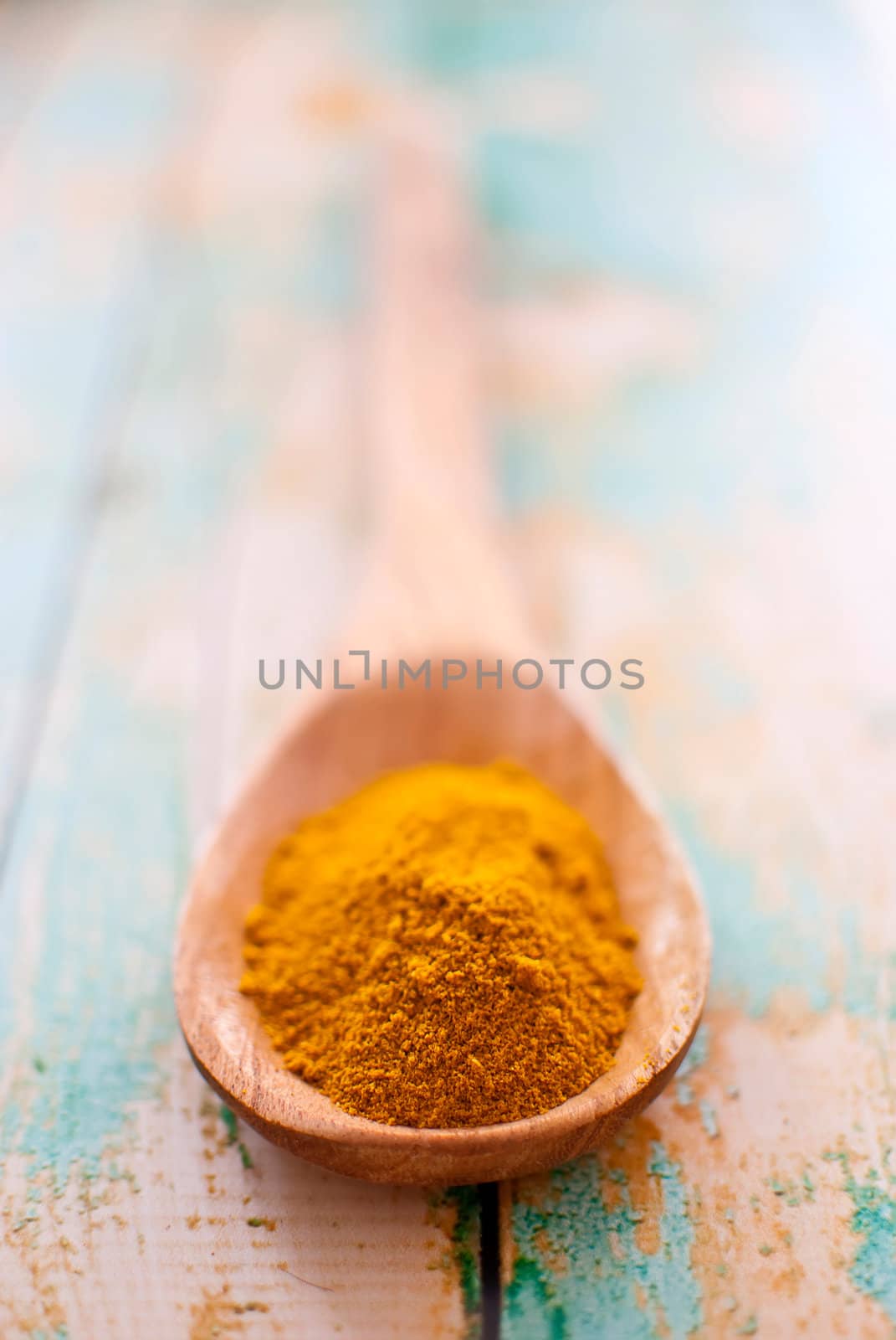 curry spice in wooden spoon over wood background - selective focus
