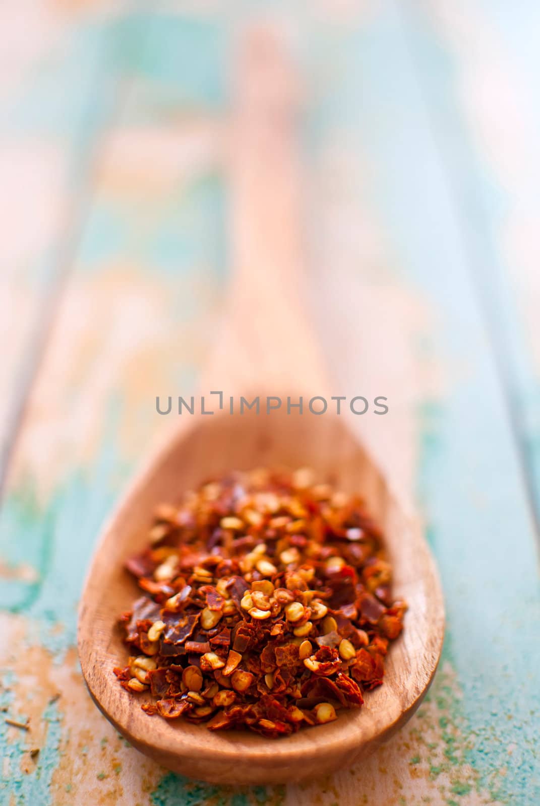 red chilli flakes in wooden spoon over wood background - selective focus
