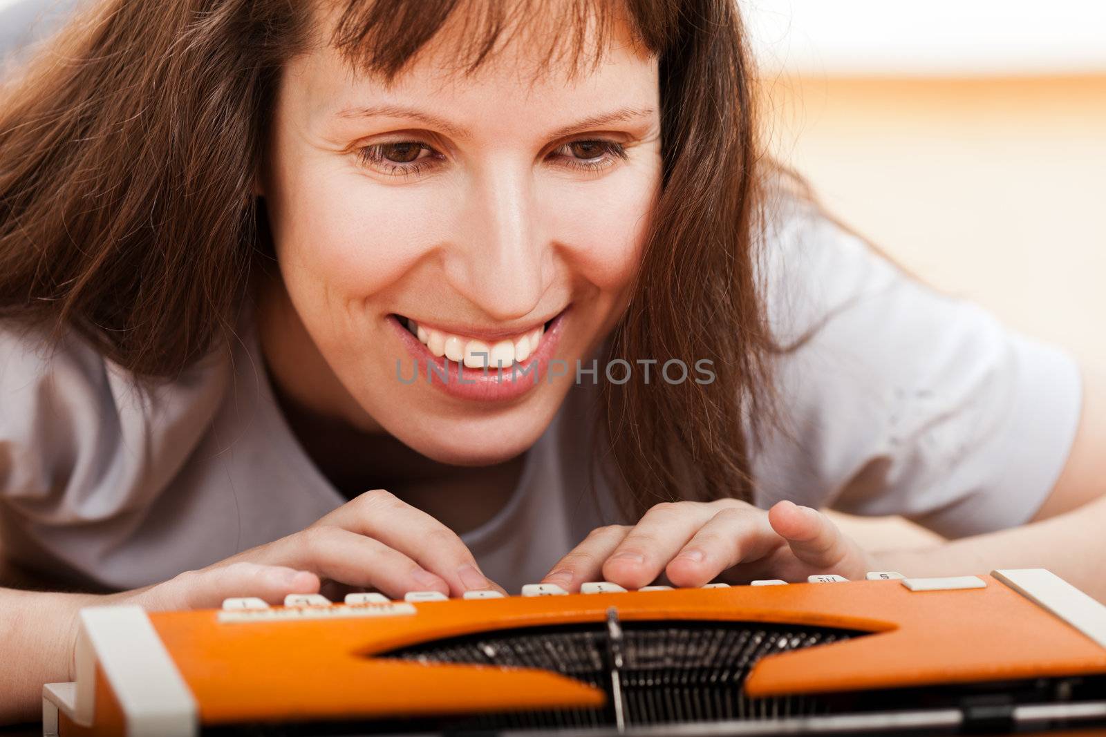 Smiling woman lying down floor typing text on old typewriter