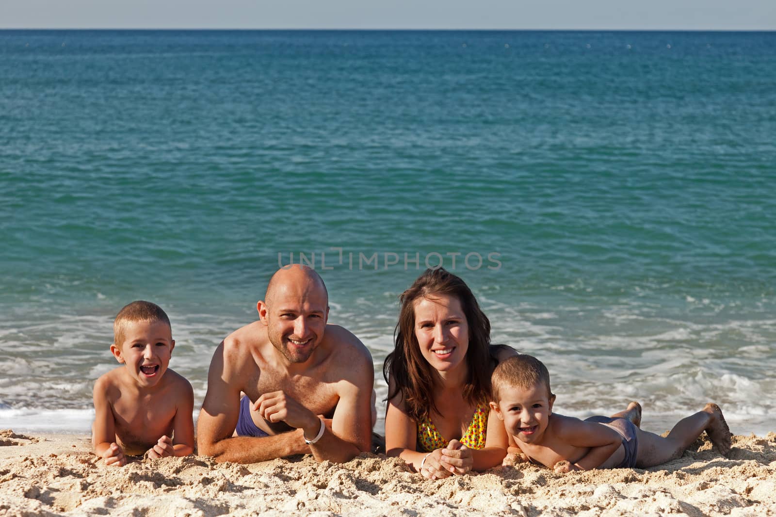 Summer vacations - happy family with two little child boy brothers playing on blue sea sand beach