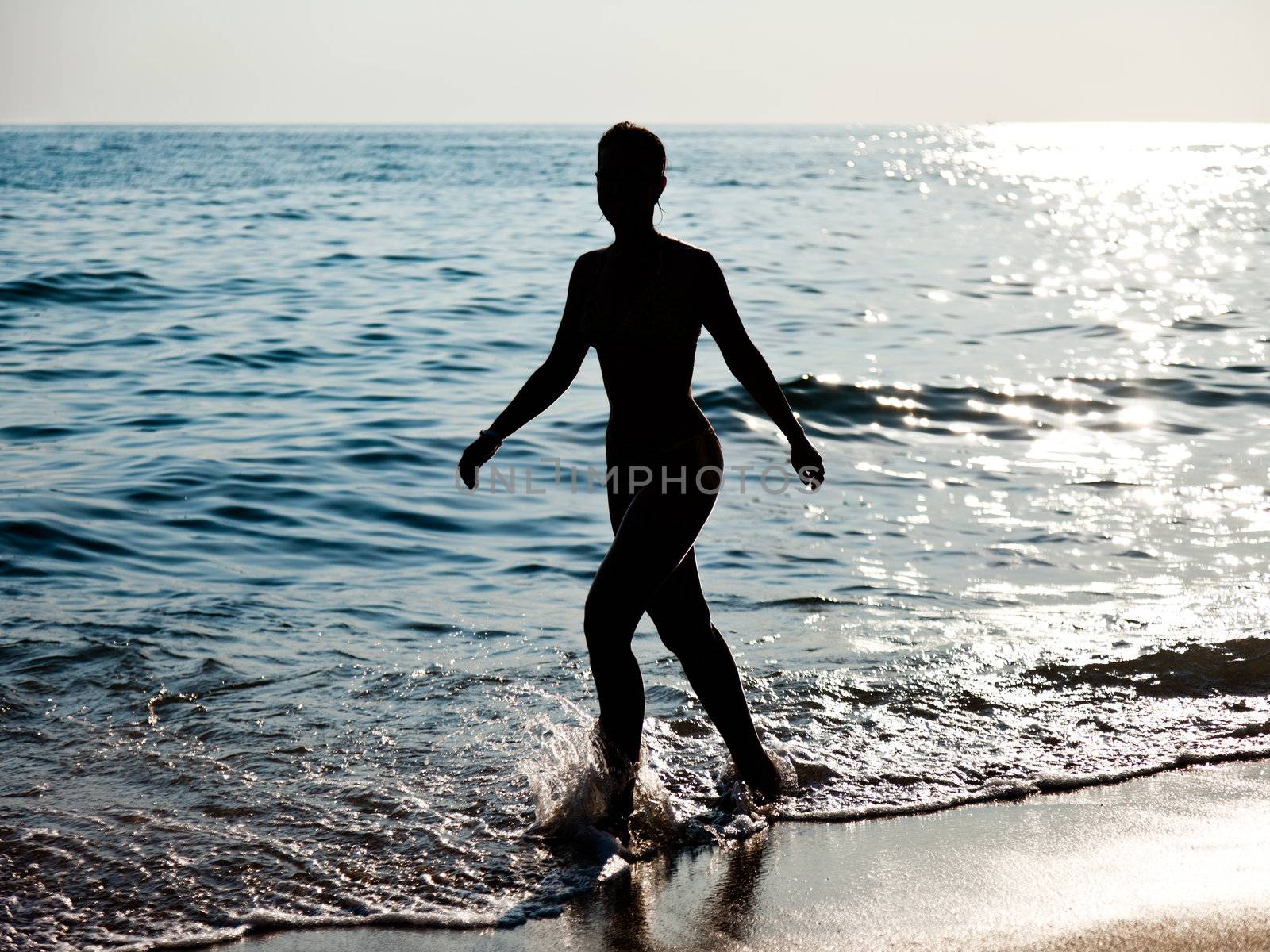 Summer vacations - beautiful slim woman silhouette walking on sea sand beach