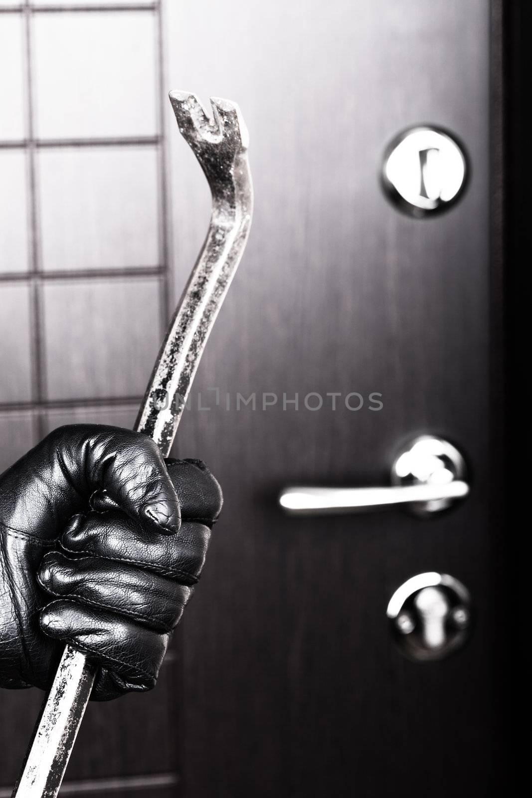 Burglar hand holding crowbar break opening door by ia_64