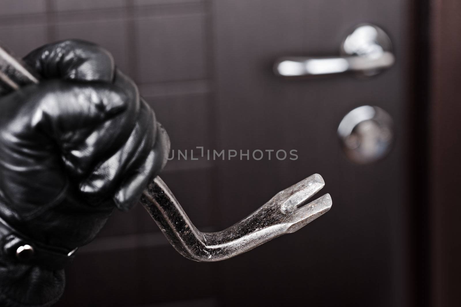 Crime scene - criminal thief or burglar hand in gloves holding metal crowbar break opening home door lock