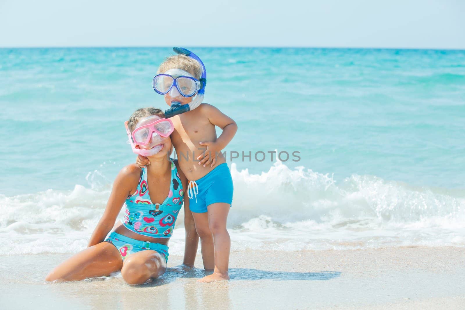 Smiling Happy brother and sister posing on a beach wearing snorkeling equipment. In the background the sea