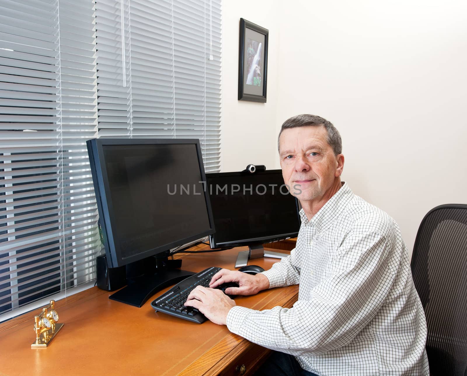 Senior executive in home office with two monitors and keyboard on leather desk and facing the camera