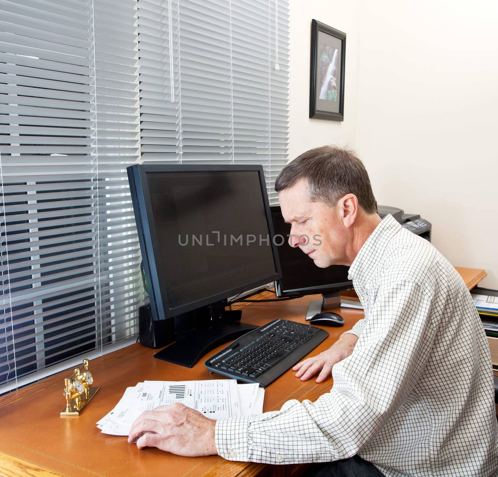 Senior executive in home office with two monitors and keyboard on leather desk and looking at paperwork on desk