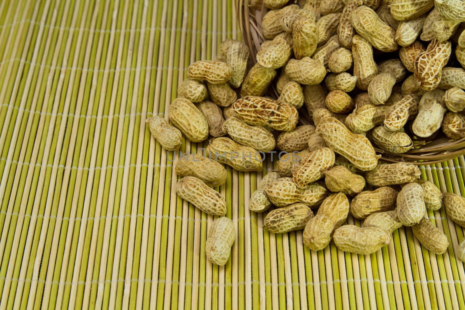 pile of groundnut spilled from a rattan basket onto a bamboo mat as background