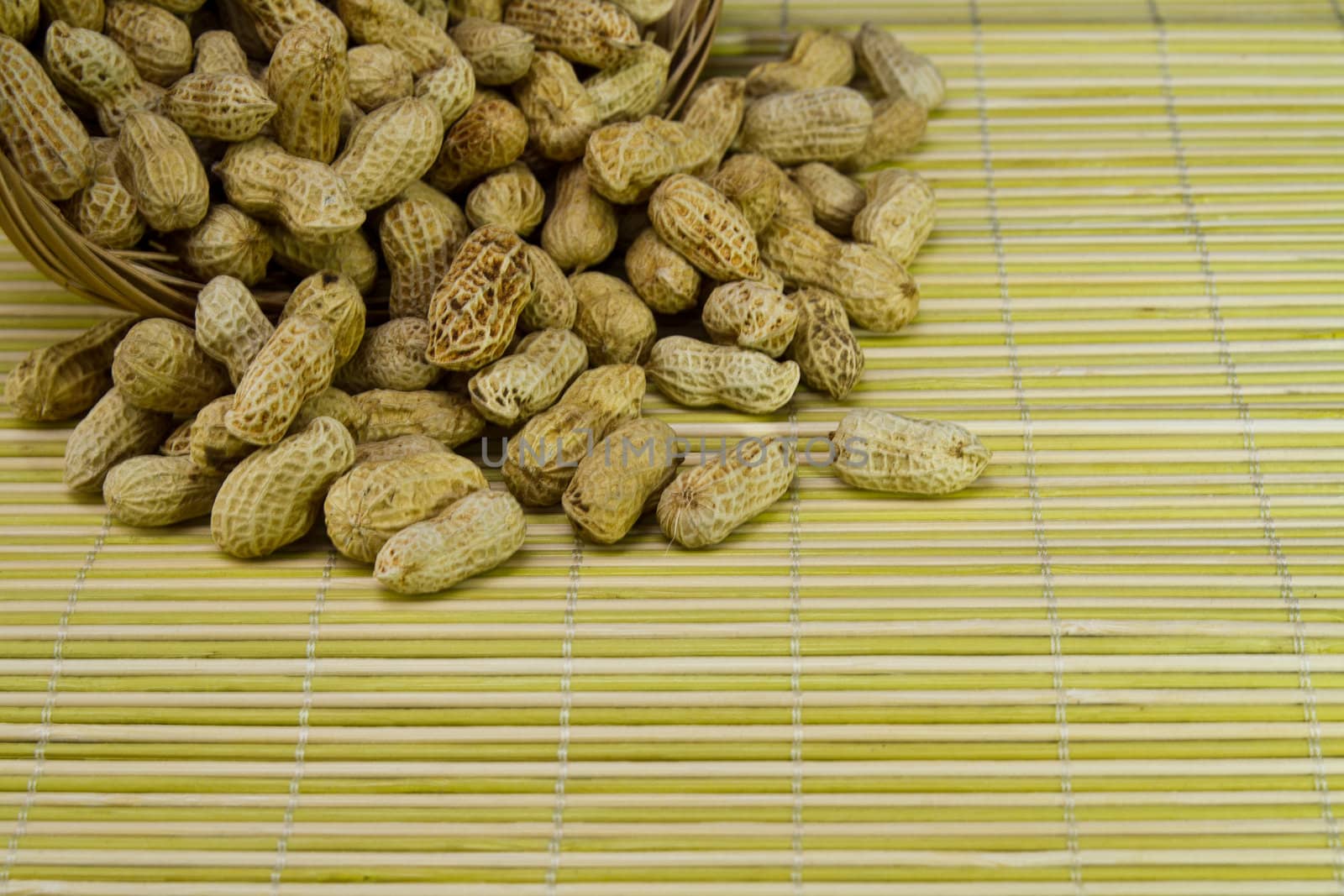 Pile of groundnut spilled from a rattan basket onto a bamboo mat in landscape orientation as background