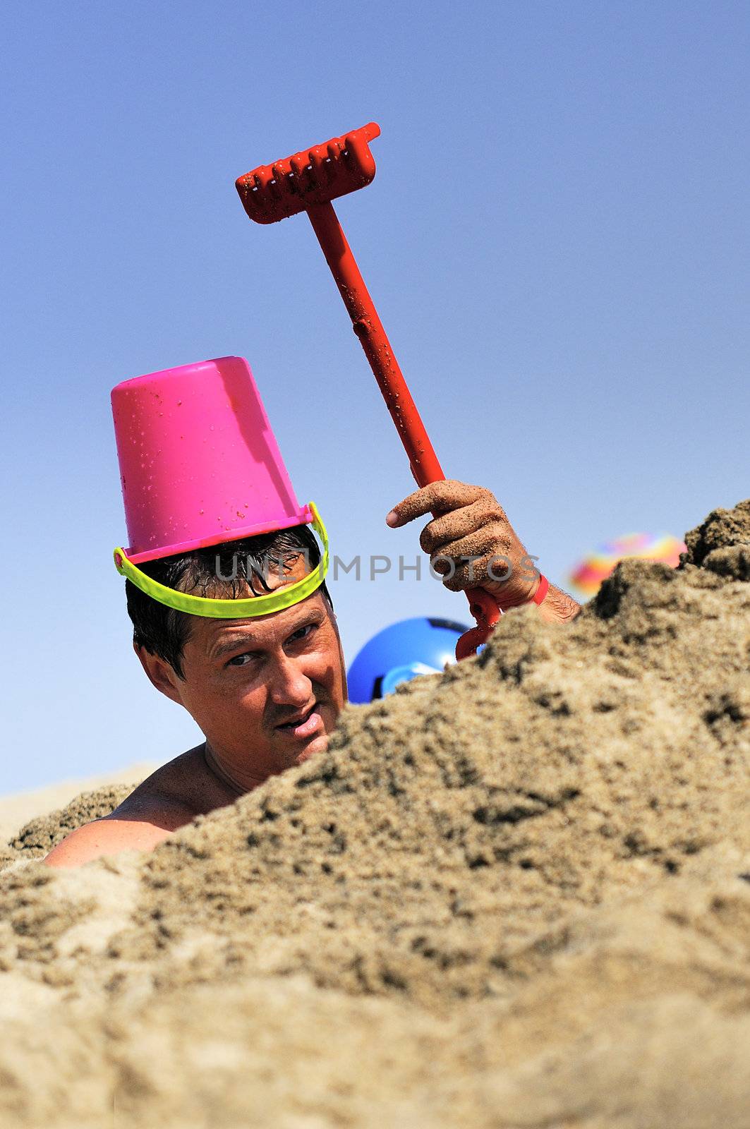 crazy man is joking on the beach in the sand with a rake and a bucket