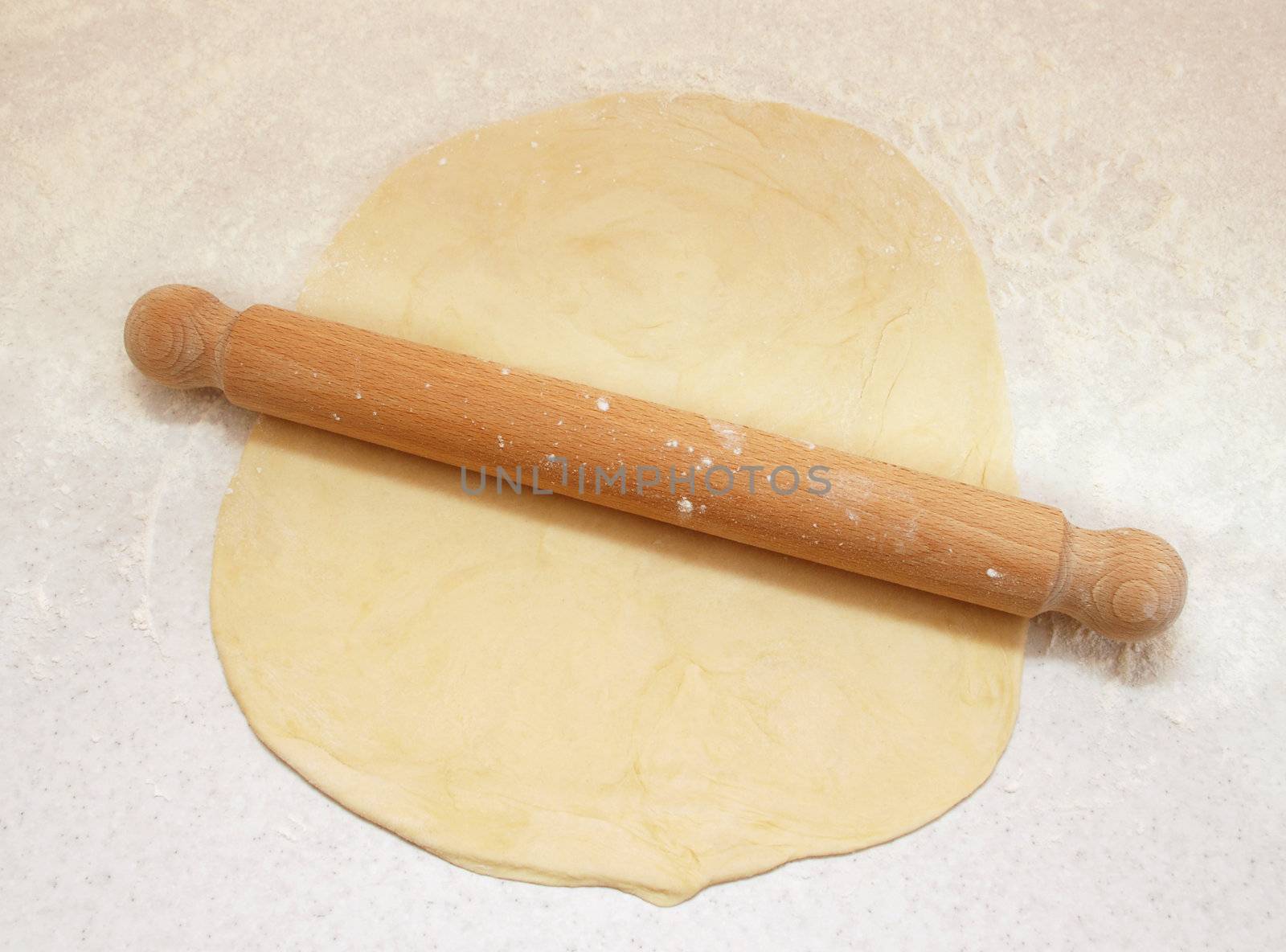 Block of freshly made pastry rolled out on a floured work surface with a wooden rolling pin