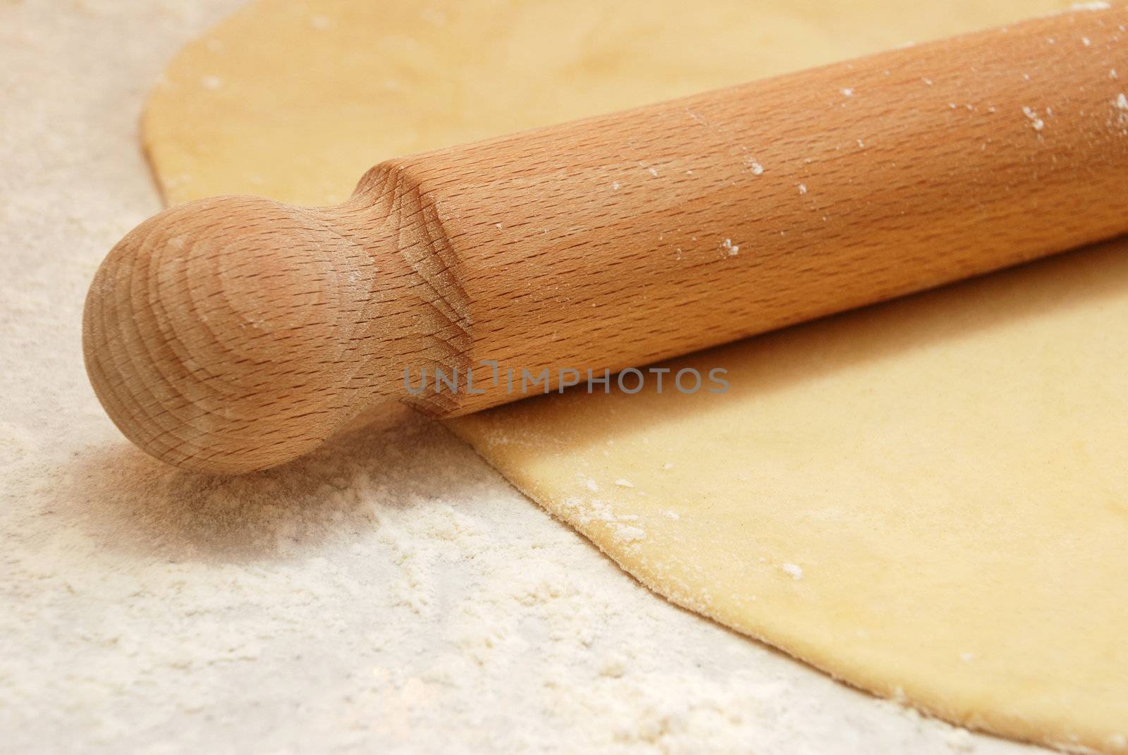 Closeup detail of a wooden rolling pin on thinly rolled out fresh pastry