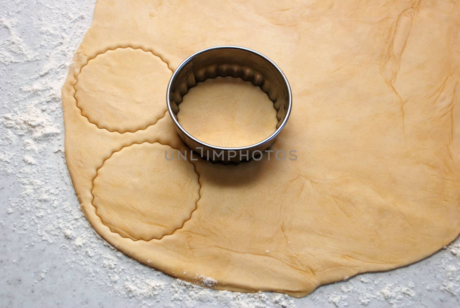 Metal cutter cutting out circles of fresh pastry for jam tarts