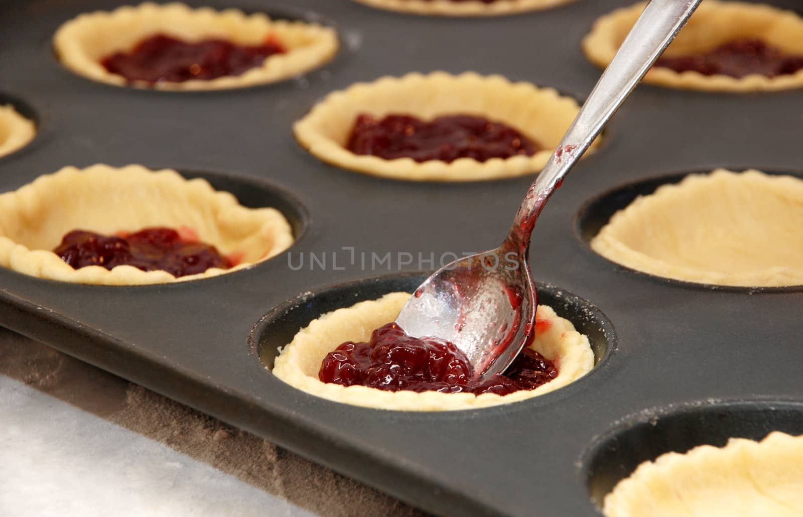 Closeup of jam tarts being filled with a metal teaspoon 