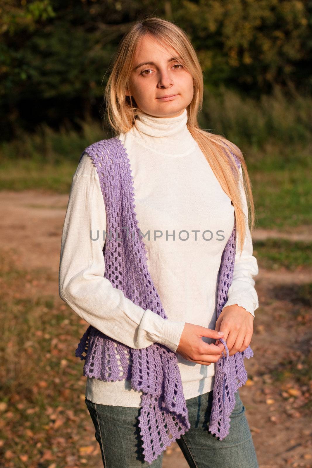 A girl in a lilac vest and white polo-neck sweater and jeans in a forest
