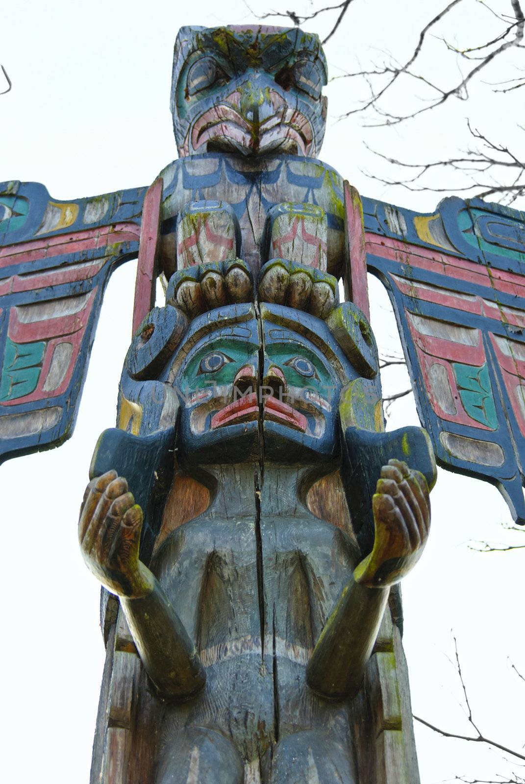 Totem pole outside on zhe background of sky and trees brunches