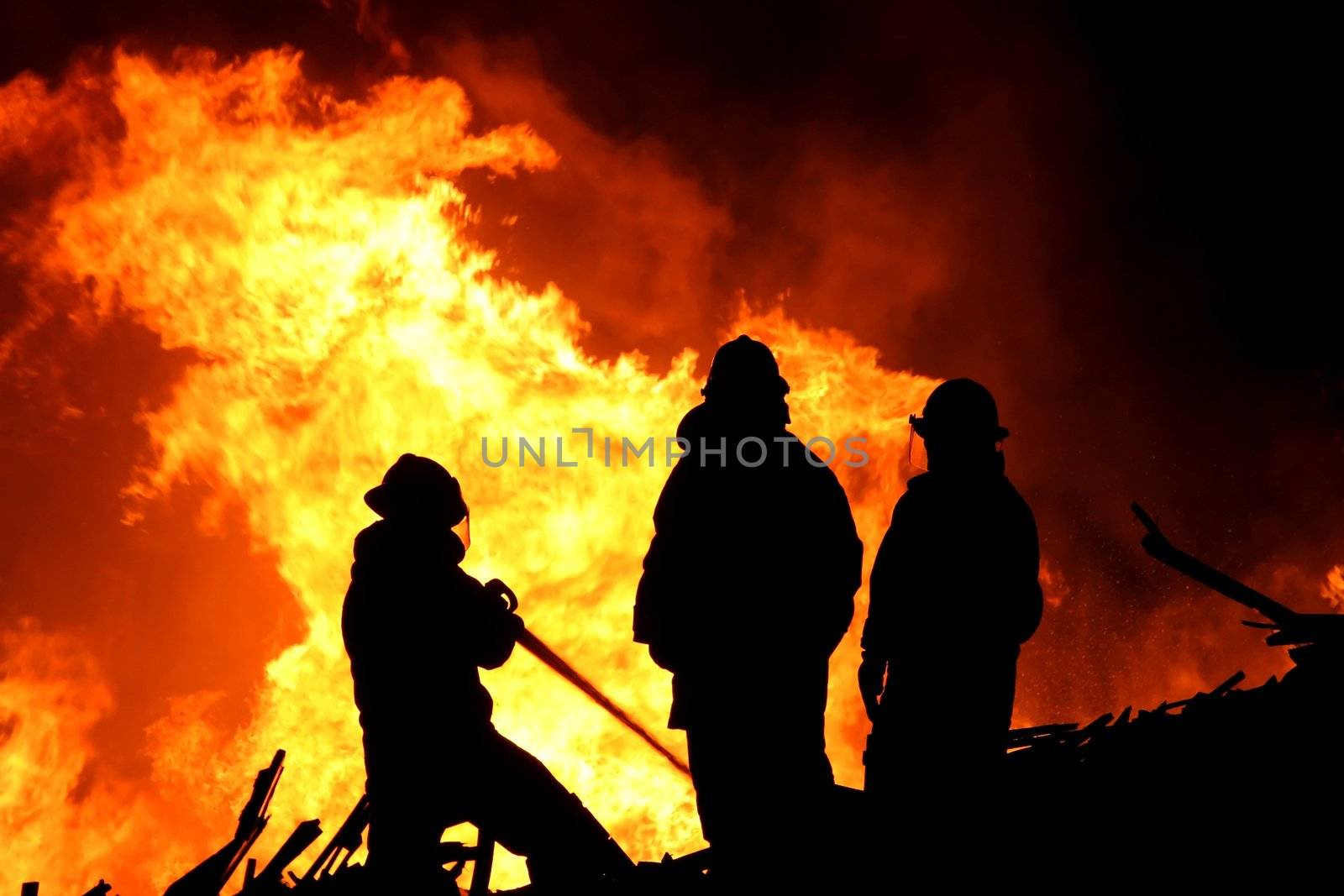 Three firemen fighting a raging fire with huge flames of burning scrap timber