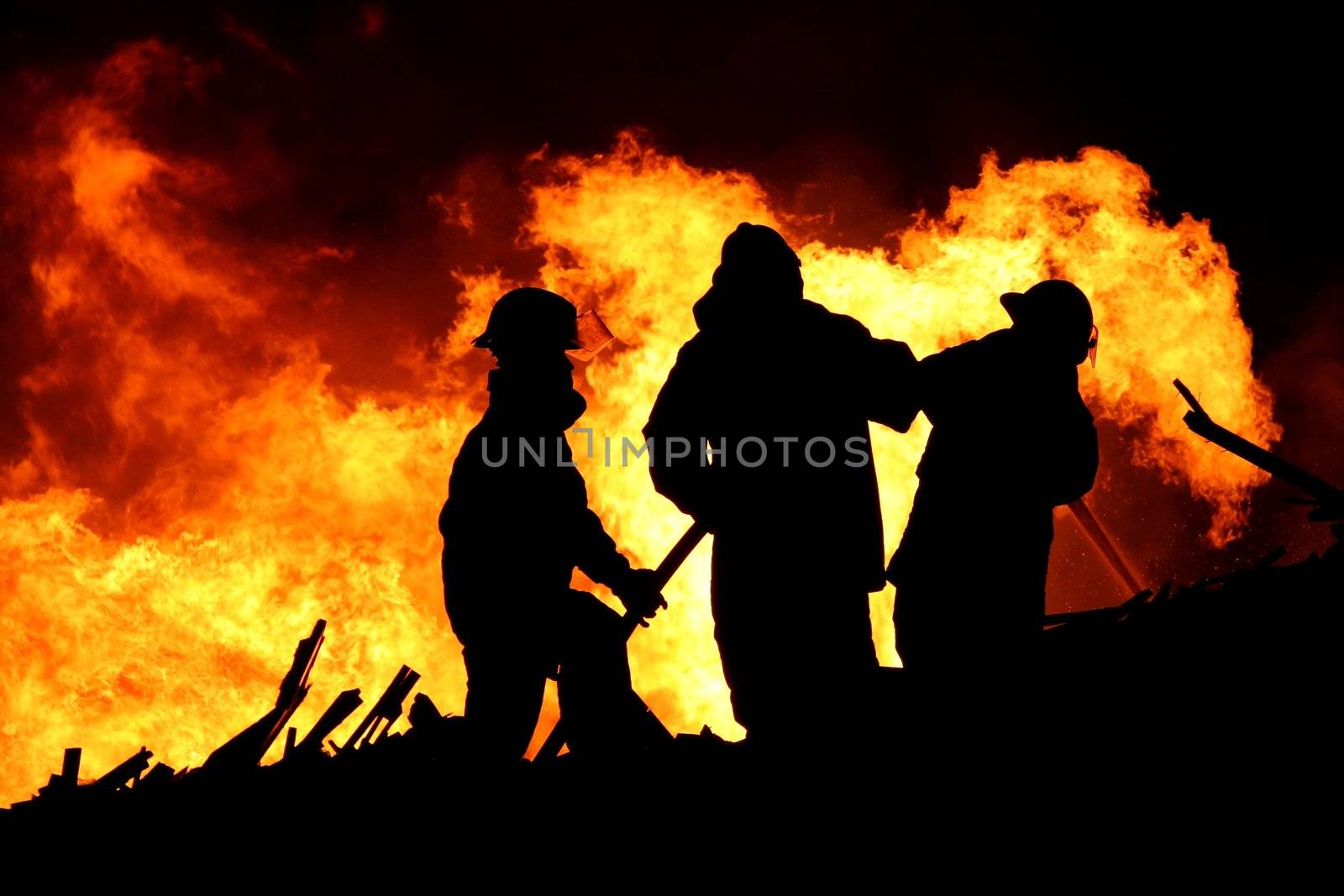 Three firemen fighting a raging fire with huge flames of burning scrap timber