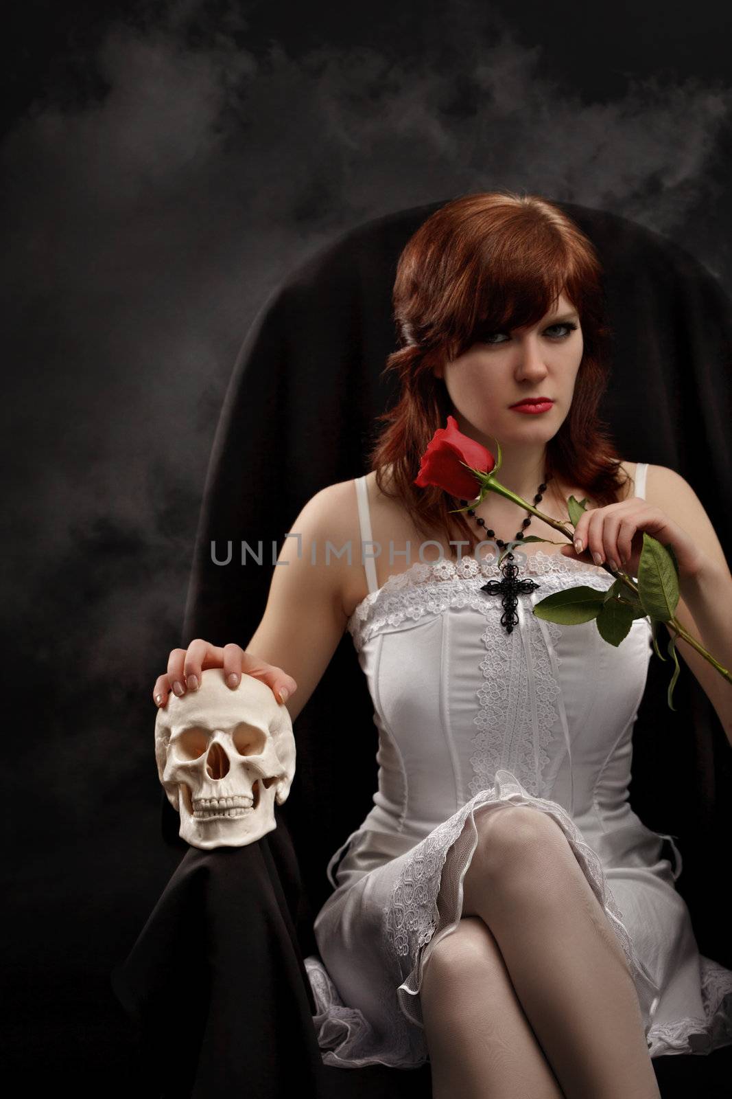 Young sexy witch sitting in a chair with a skull and rose