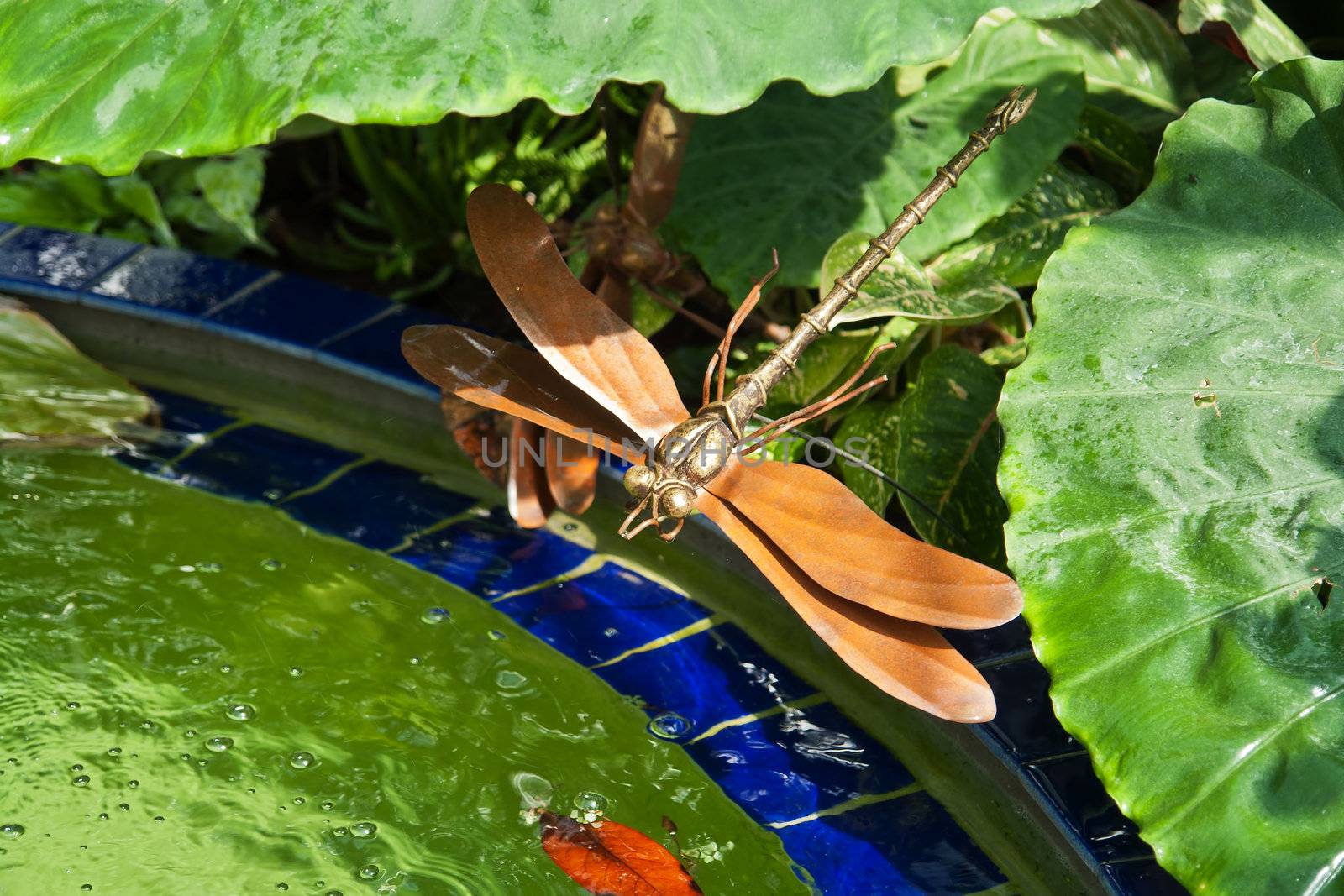A metal dragonfly statue in a beautiful lush green garden