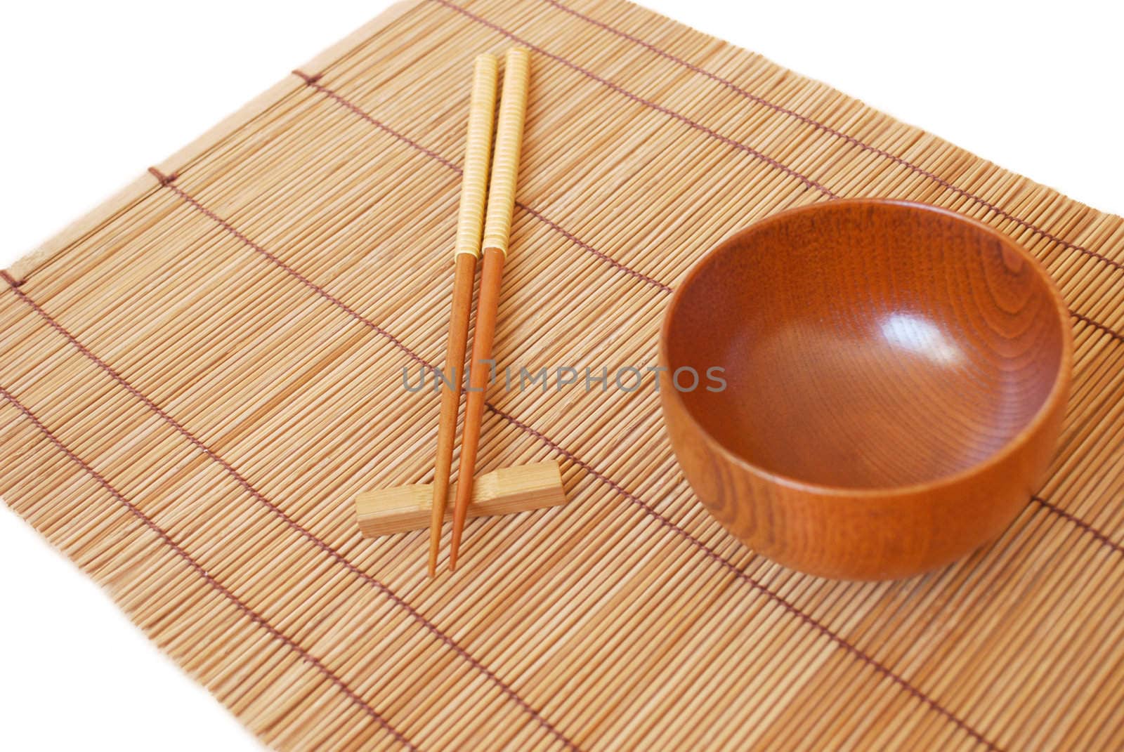Chopsticks with wooden bowl on bamboo matting background  by svtrotof