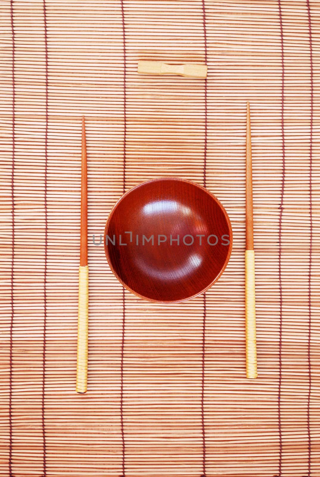 Chopsticks with wooden bowl on bamboo matting background 