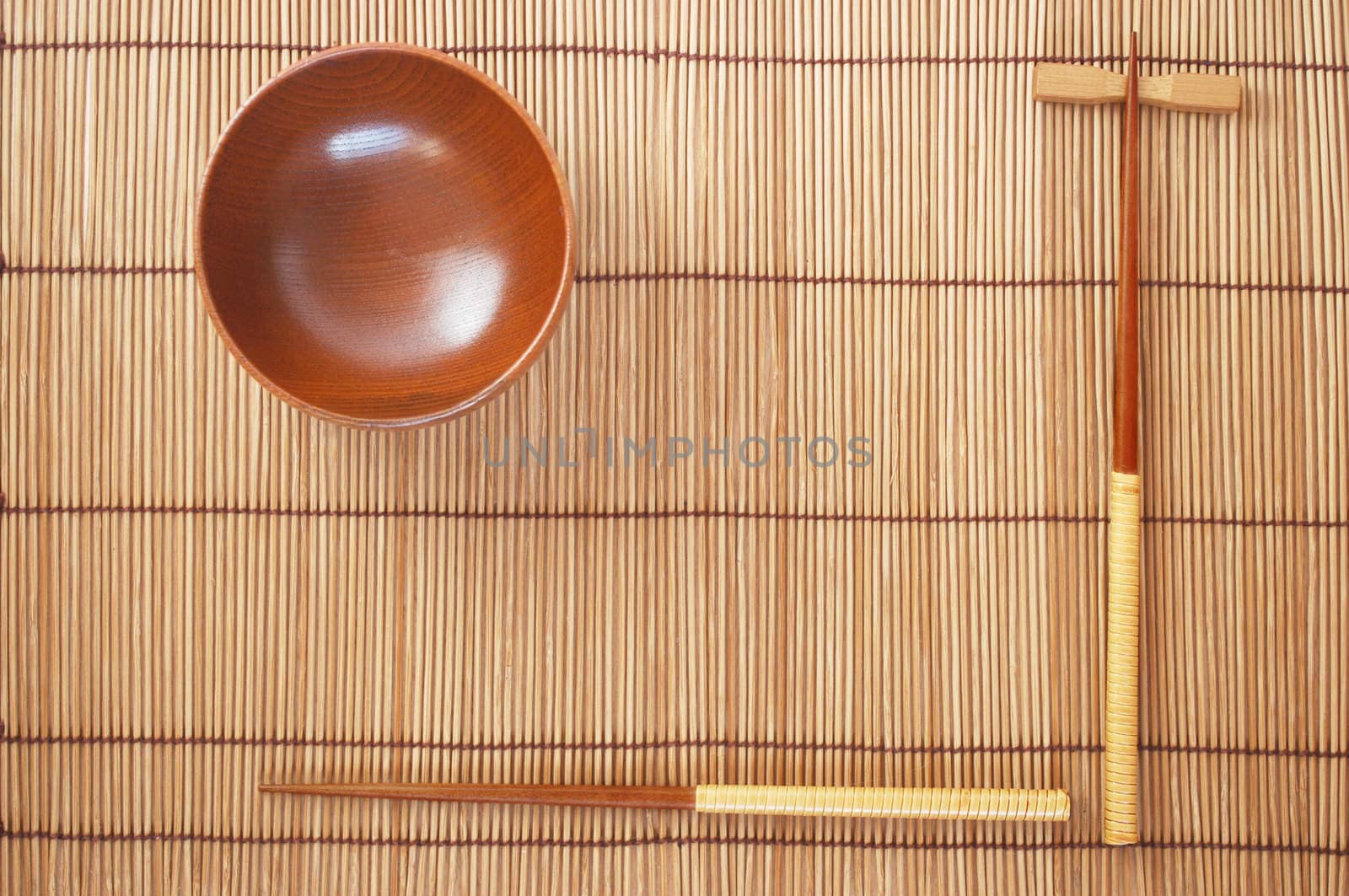 Chopsticks with wooden bowl on bamboo matting background  by svtrotof